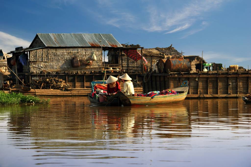 Zwei Kambodschanische Frauen auf einem Holzboot auf dem Tonle Sap See. Im Hintergrund ein Holdpier und einfache Bambushütten