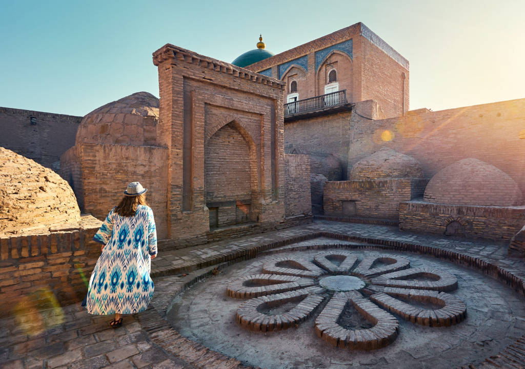 Woman tourist in ethnic dress at Inner Yard with floor in flower shape from stones near madrasah at ancient city wall at Khiva in Uzbekistan