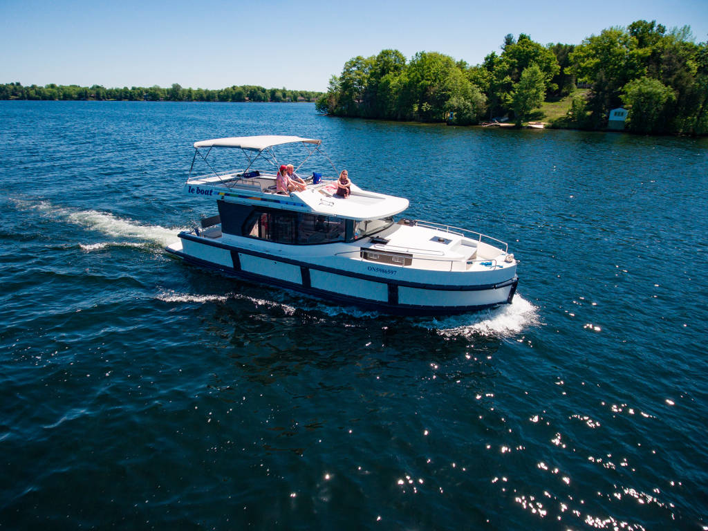 Aerial view of a lone Horizon boat cruising on the Rideau Canal, surrounded by vast water and low wooded islands.