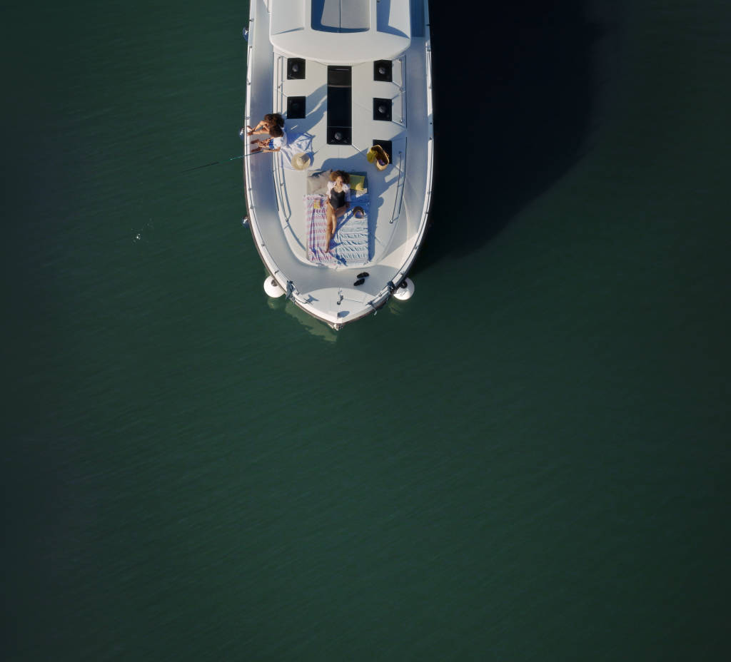 Femme alongee sur le pont avant d'un bateau Horizon pendant que deux enfants pechent du bord droit du bateau
