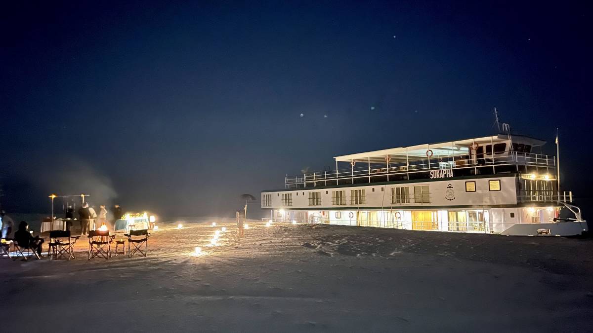 Aussenansicht des Schiffes MV Sukapha bei Nacht mit Lagerfeuer und Stühlen am Flussufer