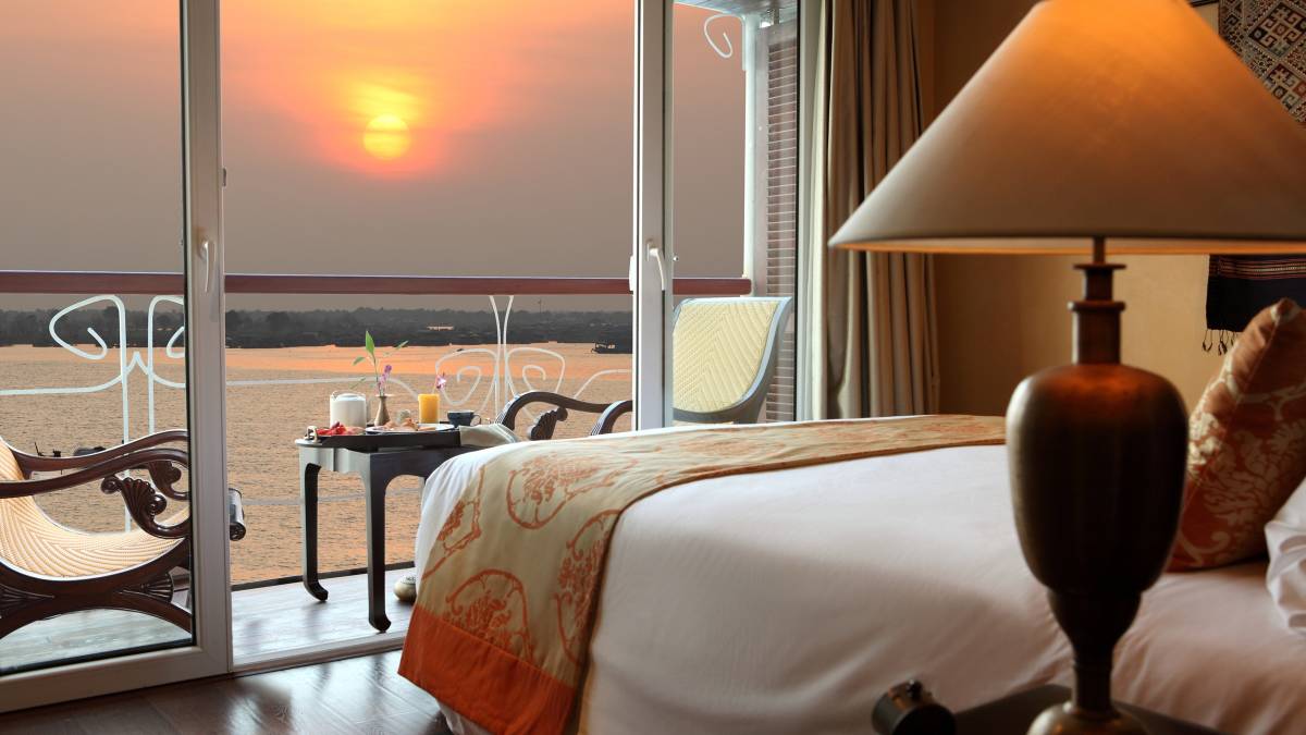 Blick durch die Kabine des Schiffs Jayavarman auf den Balkon, im Hintergrund der Mekong Fluss bei Sonnenuntergang