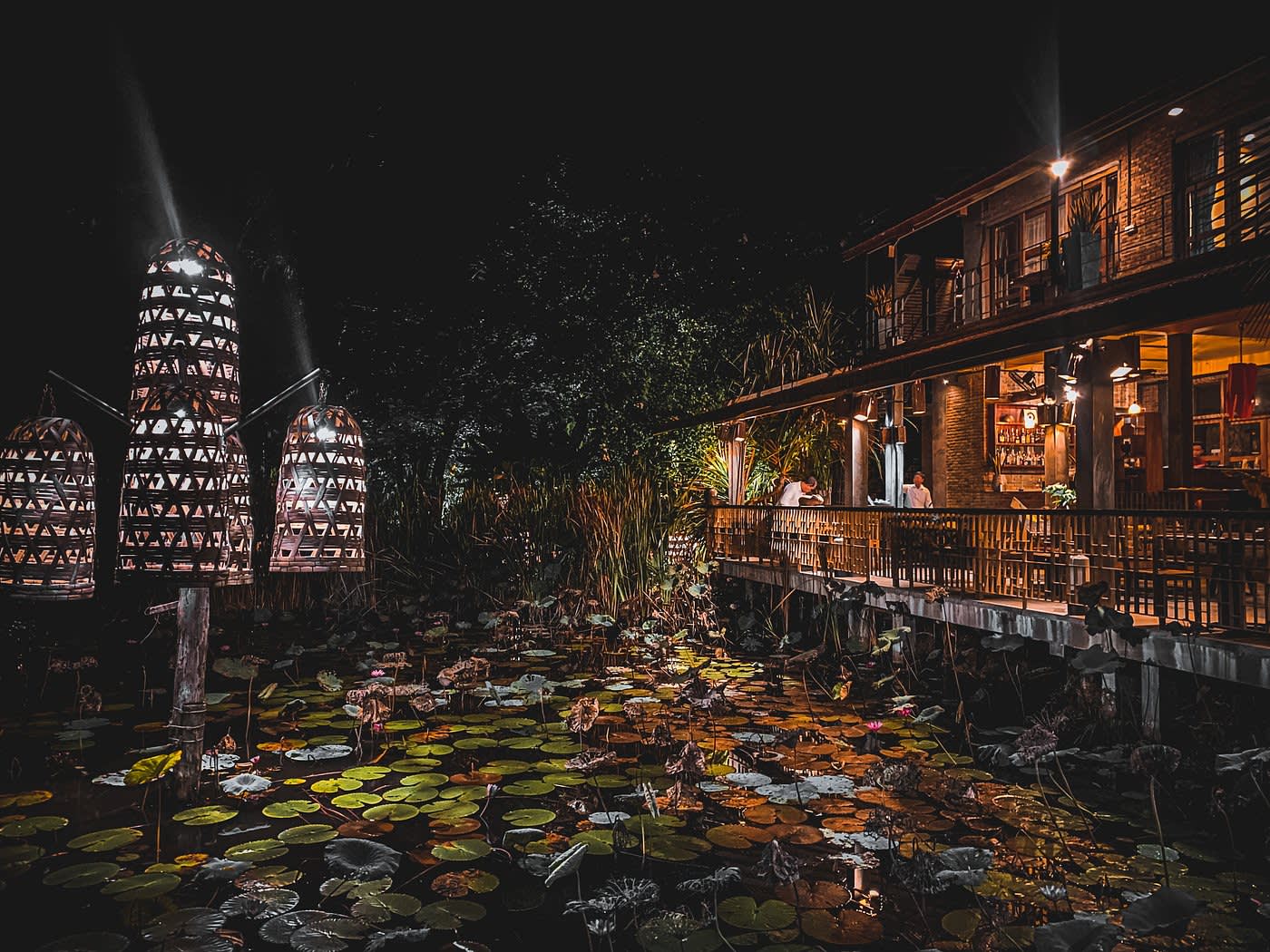 Nachtaufnahme mit Blick vom Lotusteich auf das beleuchtete Restaurantterrasse des Hotels Maisons Wat Kor in Battambang