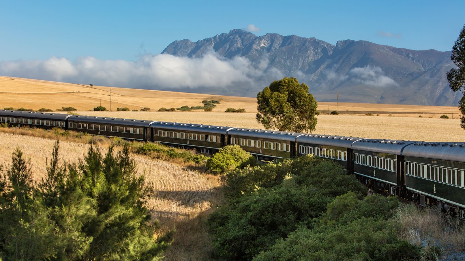 Panoramablick auf den Rovos Rail Zug in Südafrika, im Hintergrund eine schroffe Bergkette 