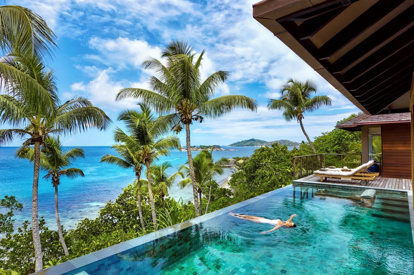 Blick auf eine im Privatpool treibende Frau im Badeanzug, im Hintergrund eine palmengesäumte Terrasse mit Liegestühlen und Blick aufs Meer, Privatinsel Félicité, Seychellen.