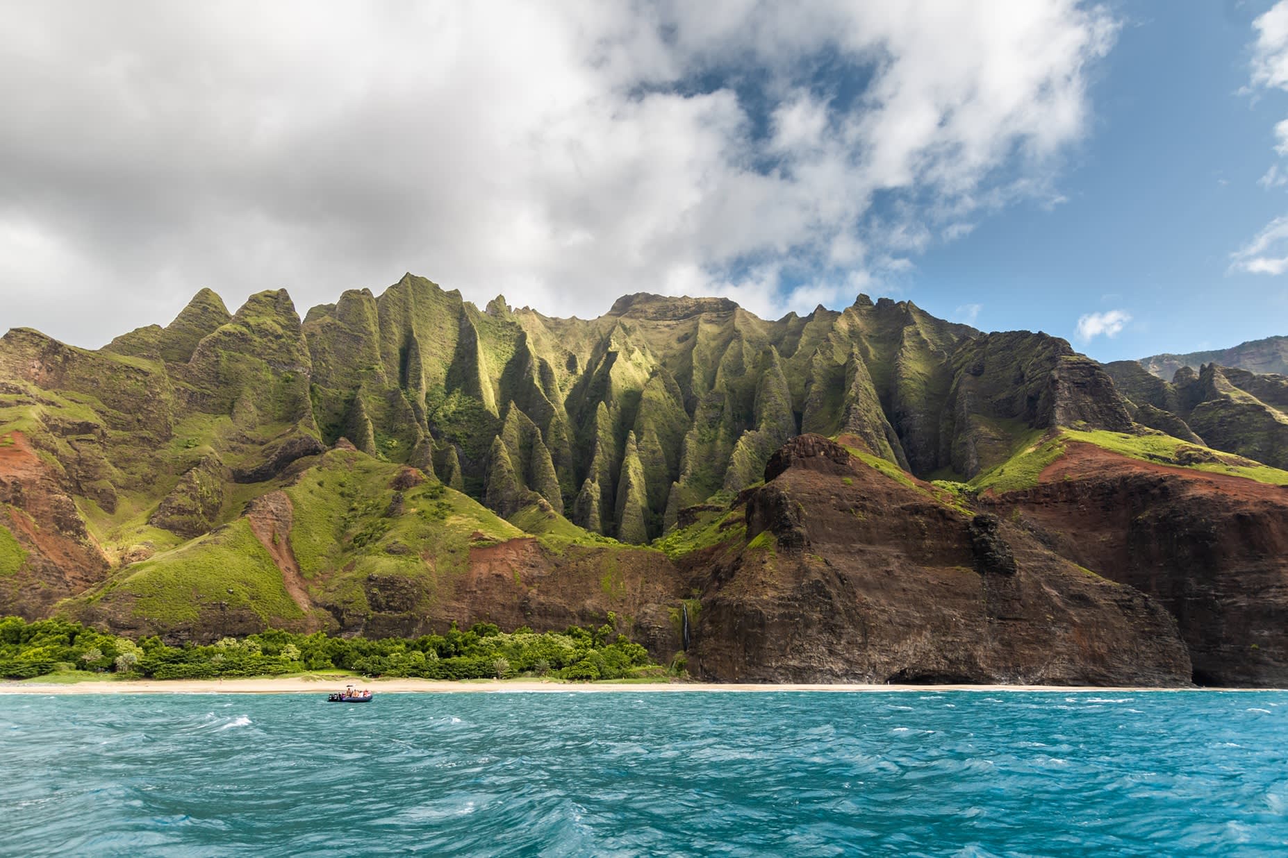 Blick vom Ozean auf die grüne zerklüftete Küste der Na Pali Coast auf Kauai