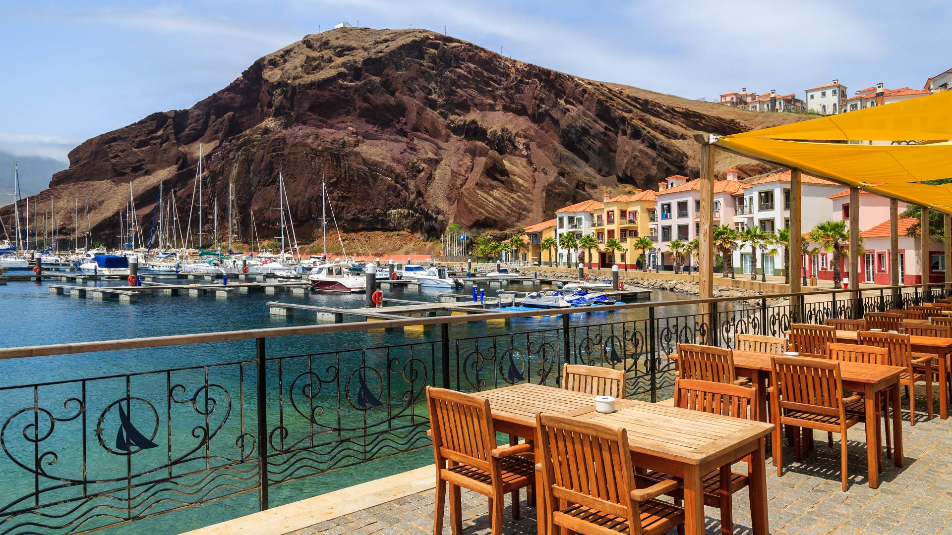 Chairs and tables of local restaurant in harbour with boats and yachts and colorful houses, Madeira island, Portugal