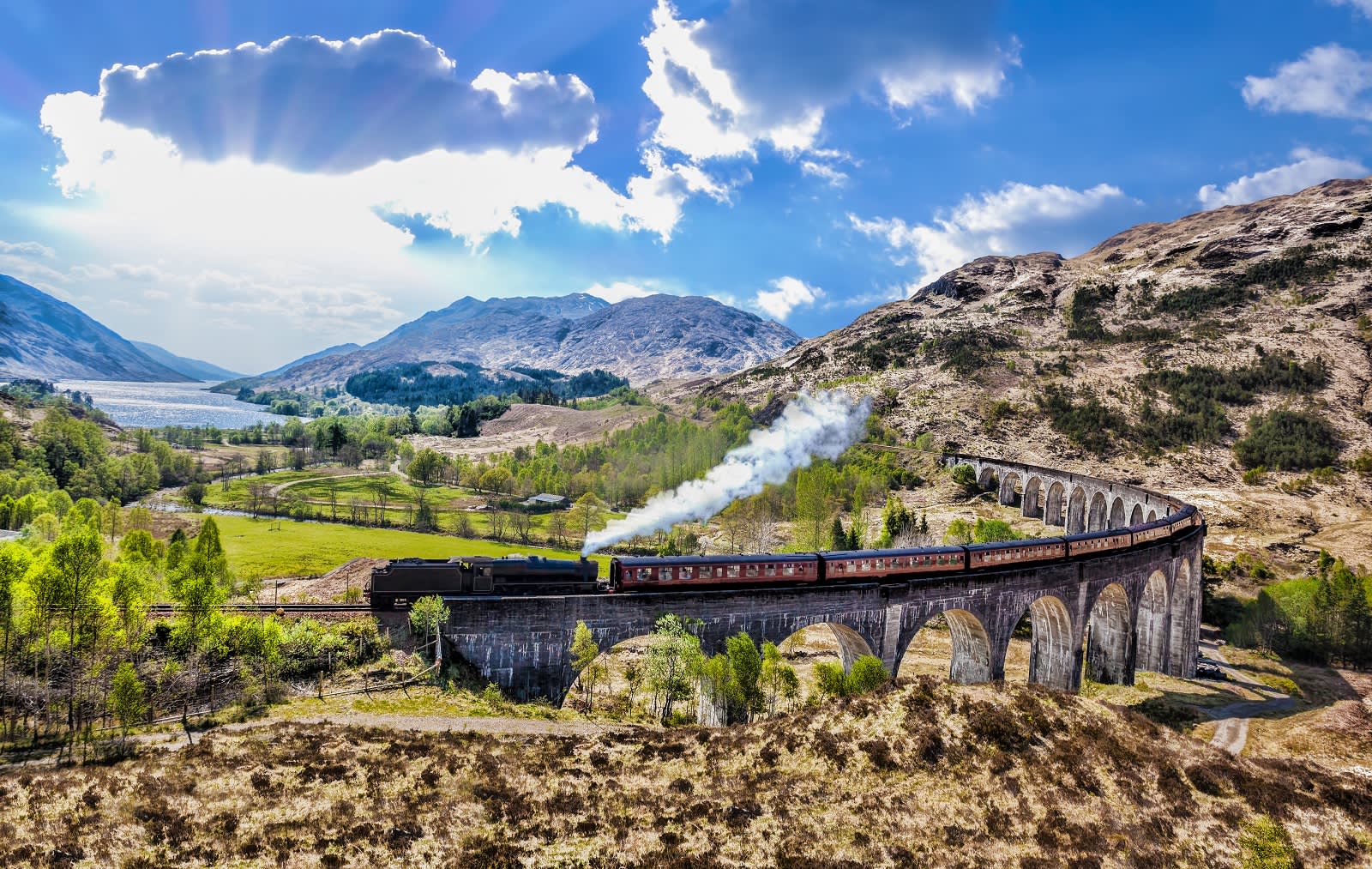 Enchanting Travels UK & Ireland Tours Glenfinnan Railway Viaduct in Scotland with the Jacobite steam train against sunset over lake