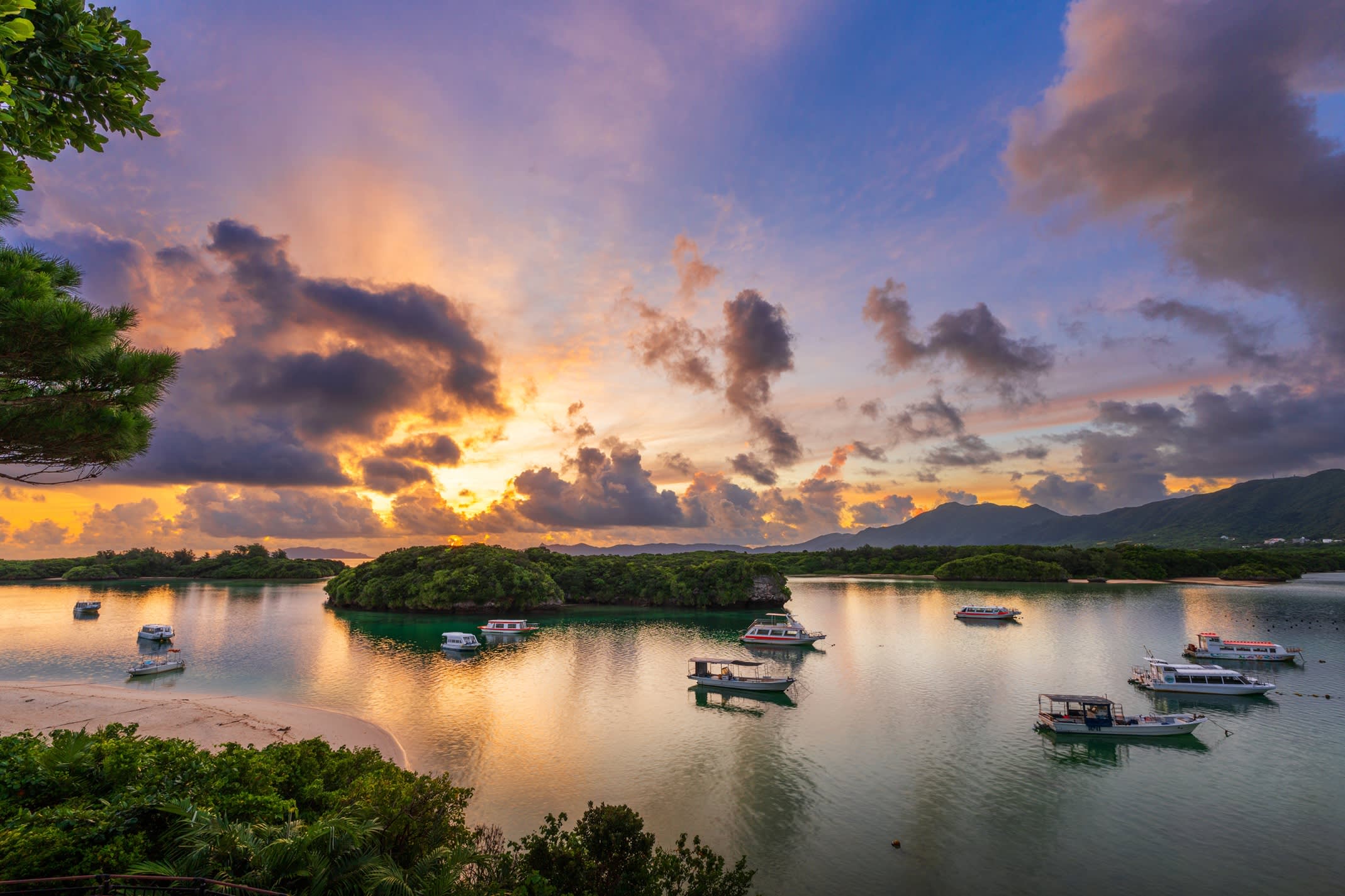 Kabira-Bucht auf Ishigaki, Japan, bei Sonnenaufgang mit buntem Himmel, ankernden Booten und grünen Inseln.