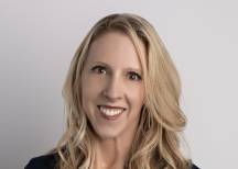 Amanda Wright, smiling woman with long blonde hair, wearing a navy top, gold earrings, and a beaded pendant necklace.