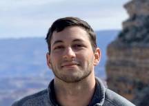 Ben Burtis smiling outdoors in a gray Patagonia fleece, with rocky canyon landscape in the background.