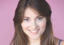 Reagan Lewis, a young woman with long brown hair and blue eyes, smiling against a pink background.