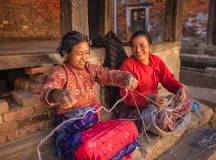 Nepali women spinning a wool in front of the house.
