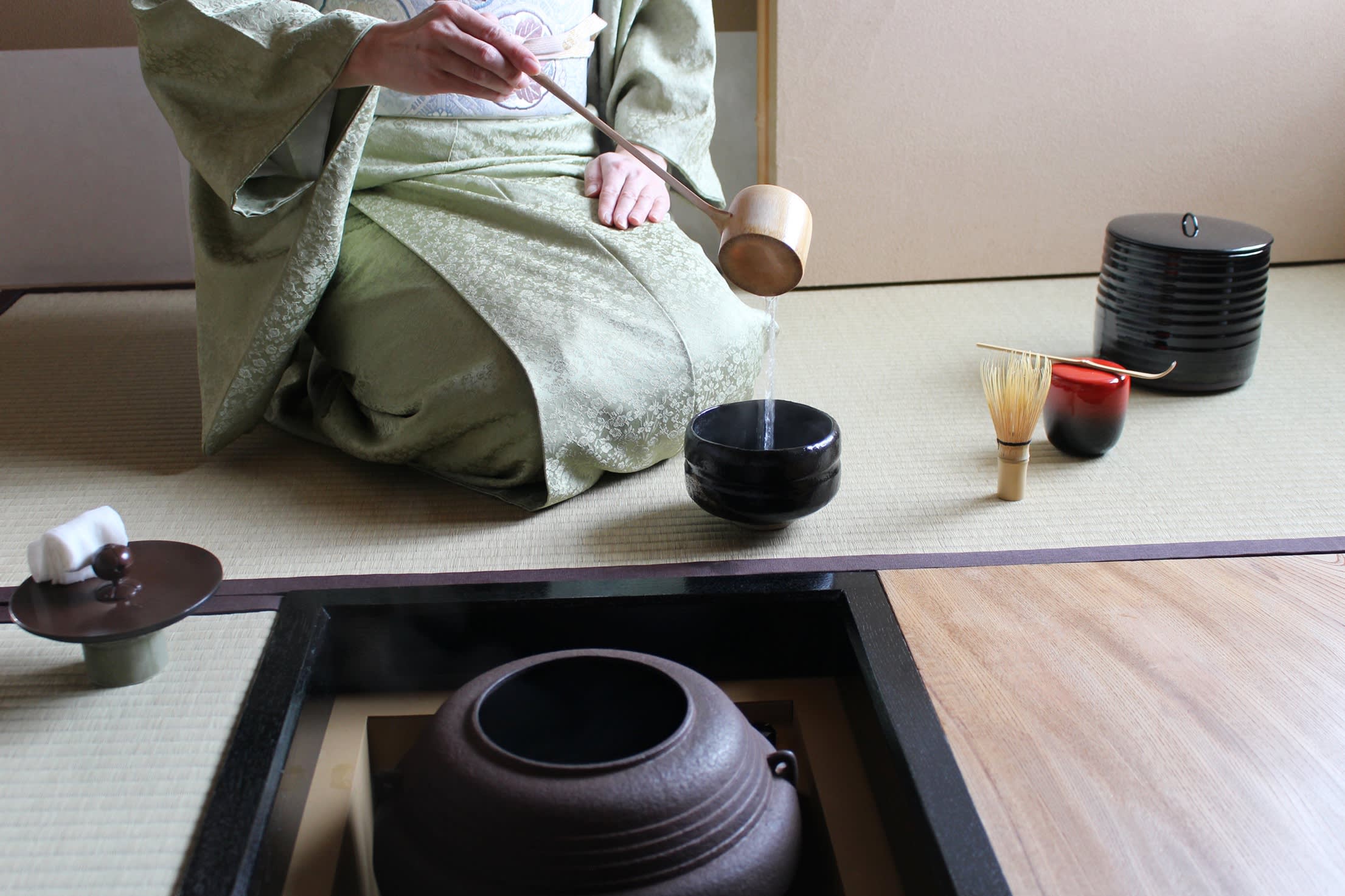 Eine in einem Kimono gekleidete Frau, die in einem japanischen Teeraum Matcha-Tee serviert.