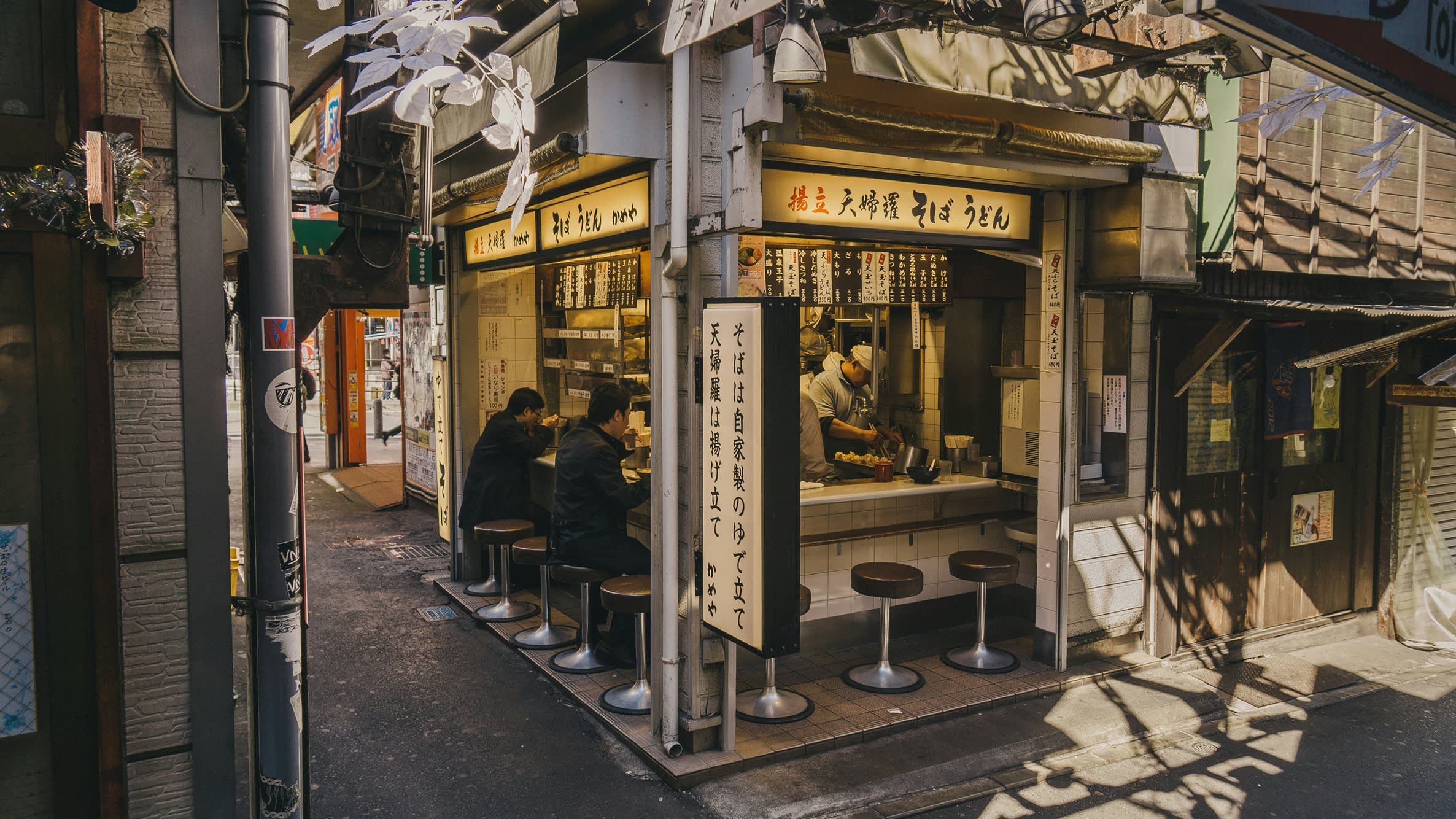 Zei Männer, die an einer Theke eines Straßenrestaurants in Japan sitzen und essen. 