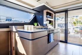 Moorings 534PC galley with a cooktop, oven and overhead shelving, opening to the cockpit through a sliding door.