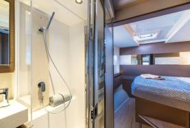 Head with glass shower enclosure and basin aboard a Moorings 534PC, with a cabin berth and overhead hatch beyond.
