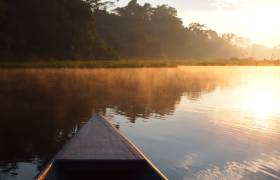 The front of a small boat navigating the Tambopata river during sunrise with reflection of the sun in the water in the Amazon rainforest in Peru