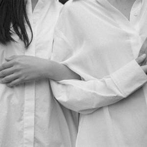 Three people in white button-down shirts embracing, arms wrapped around each other, shot in black and white.