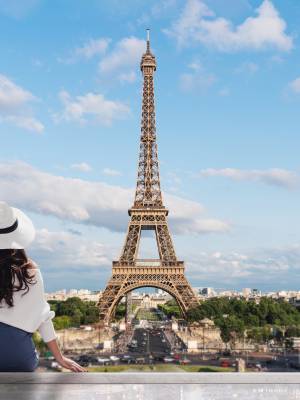 Young traveler woman in white hat looking at Eiffel tower, famous landmark and travel destination in Paris, France in summer