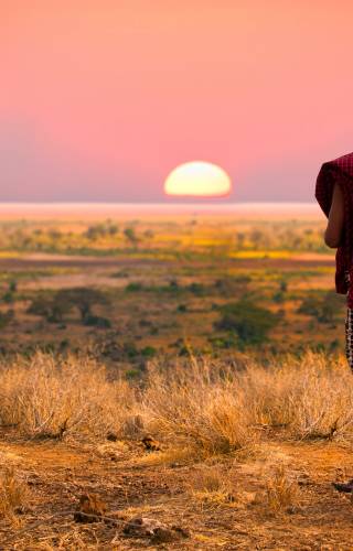 Massai man wearing traditional blankets overlooks Serengeti in Tanzania