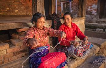 Nepali women spinning a wool in front of the house.