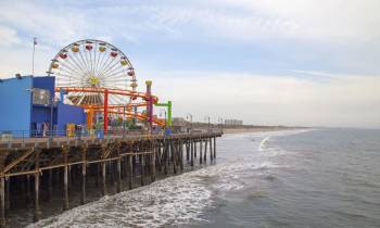 a close up of a pier next to a body of water with Santa Monica Pier in the background