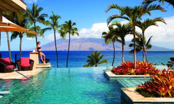 A woman standing next to an infinity pool with palm trees surrounding it