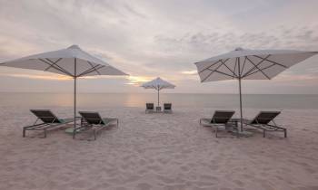 a couple of lawn chairs sitting on top of a sandy beach