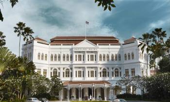 a large white building with trees in the background with Raffles Hotel in the background