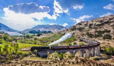 Glenfinnan Railway Viaduct in Scotland with the Jacobite steam train against sunset over lake