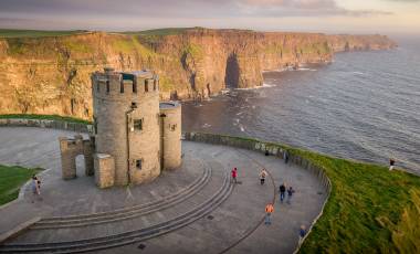 Cliffs of Moher at the west coast of Ireland with a little castle during sunset people tourists
