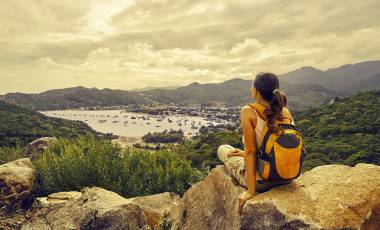 Woman traveler looks at the edge of the cliff on the sea bay of mountains in the background