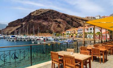 Chairs and tables of local restaurant in harbour with boats and yachts and colorful houses, Madeira island, Portugal