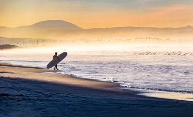 Early morning fog shrouds the coastline as this surfer enters the water in Coronado, California