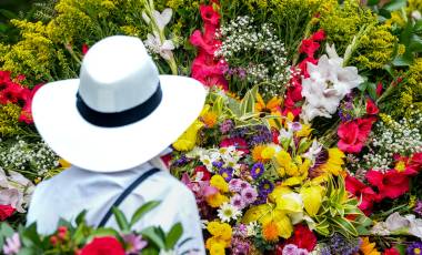 Traditional Colombian silletero wearing a white hat preparing a colorful floral arrangement during the Medellin Flower Festival parade
