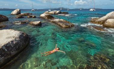 Woman swimming at The Baths in the BVI with boats in the background