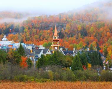 Blick auf die Kirchturmspitze des Dorfes Mont Tremblant vor der Kulisse eines nebelverhangenen Herbstwaldes
