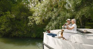 Couple sightseeing from the bow of their boat, immersed in nature and river scenery.