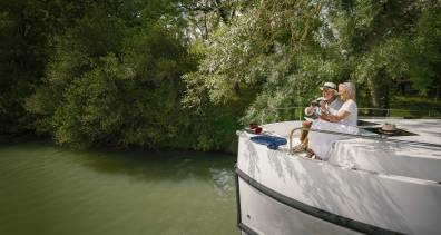 Couple birdwatching together from the front of their canal boat, surrounded by lush green forest.