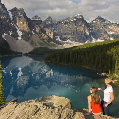 Two women standing in front of a lake with a backdrop of beautiful mountains