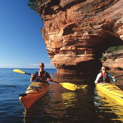 a group of people standing next to a body of water with Apostle Islands in the background