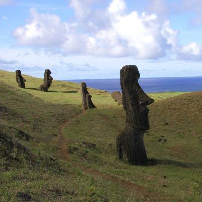 a group of people walking on a grassy hill with Easter Island in the background