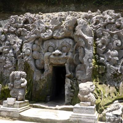 a stone statue in front of a large rock with Goa Gajah in the background