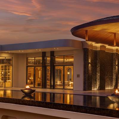 Anantara Koh Yao Yai Resort exterior at sunset, with fire bowls, reflecting pool, and warm-lit interiors under a curved wooden roof.