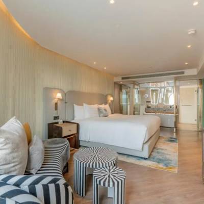 Stylish hotel room at The Salil Riverside Bangkok with striped sofa, king bed, bold black-and-white stools, and open bathroom.