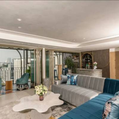 Elegant hotel lounge at The Salil Riverside Bangkok with teal and grey sofas, marble coffee table, bar area, and city views.