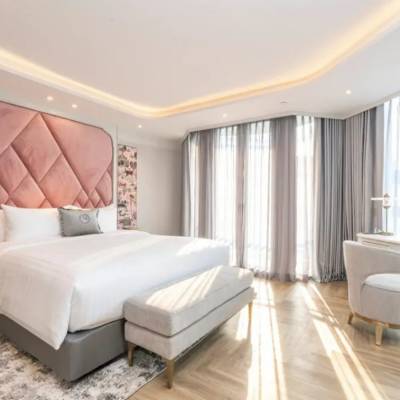 Elegant hotel room at The Salil Riverside Bangkok with a tall pink quilted headboard, king bed, hardwood floors, and floor-to-ceiling windows.