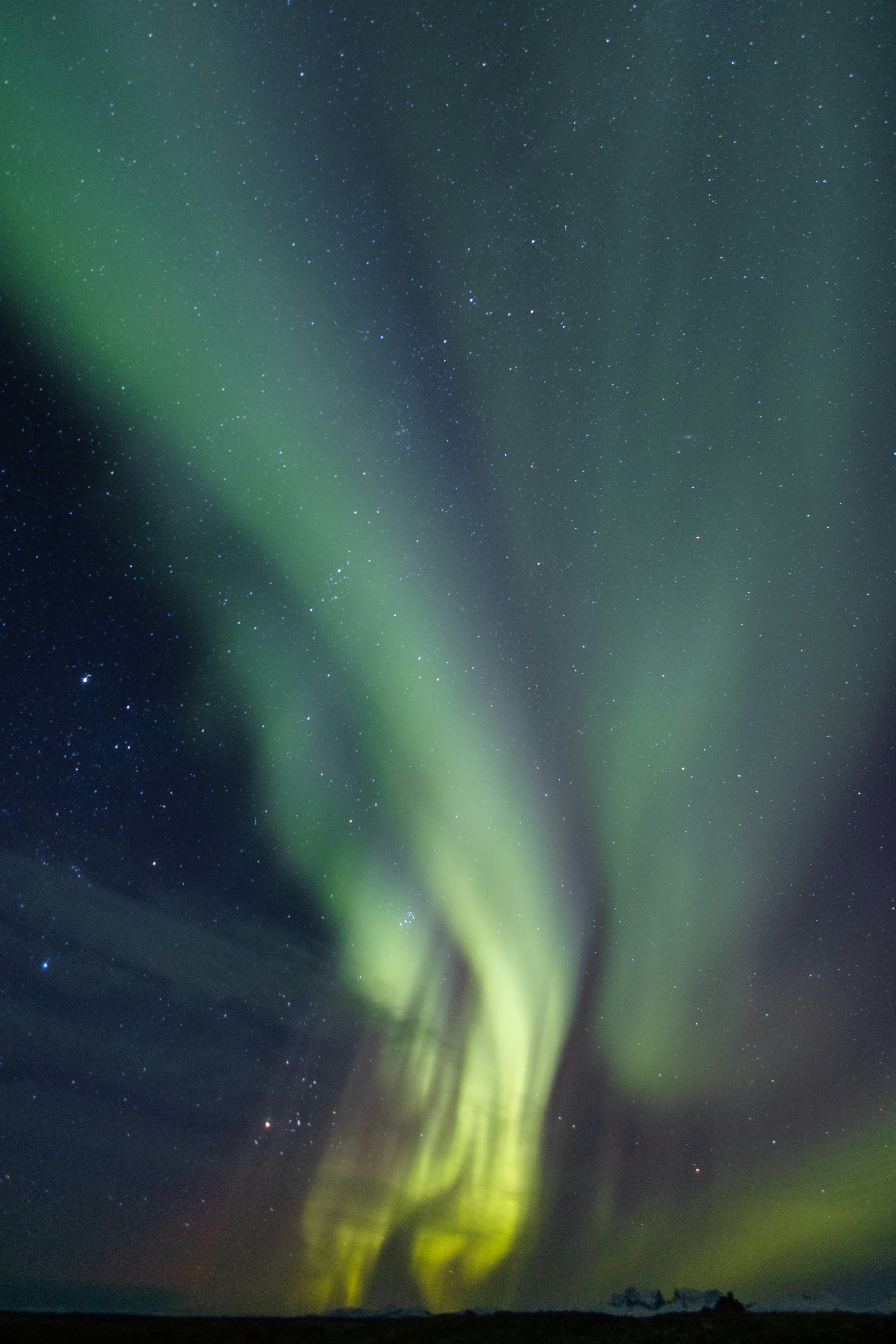 Vivid green and yellow aurora borealis swirling across a starry night sky above a dark horizon.