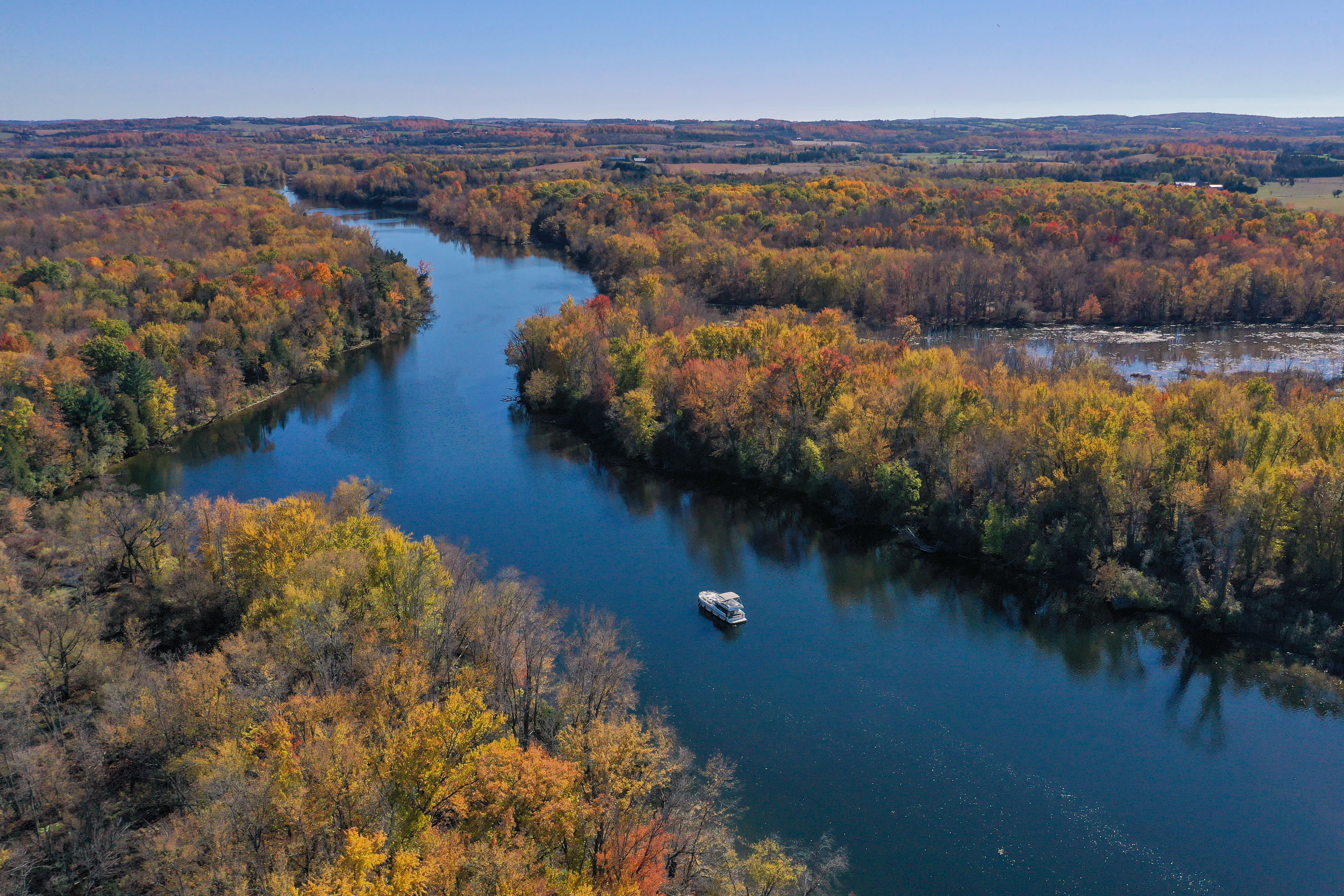 A Le Boat canal boat alone on a winding stretch of the Trent‑Severn Waterway, surrounded by brilliant autumn forest.